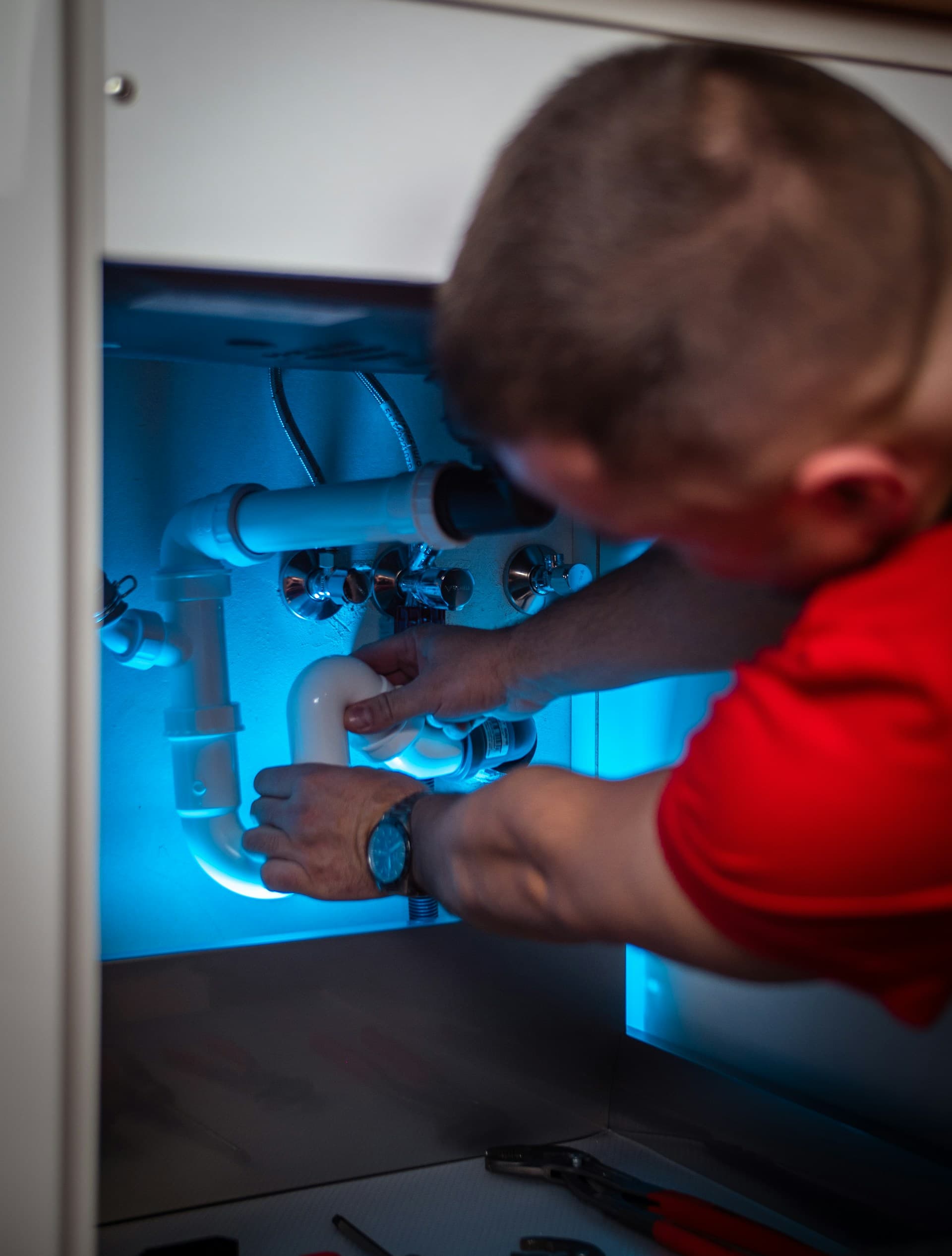 Ein Installateur arbeitet an Rohren unter einem Waschbecken